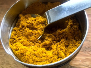 Gewürzbehälter mit gelbem Currypulver, in dem ein Metalllöffel steckt.